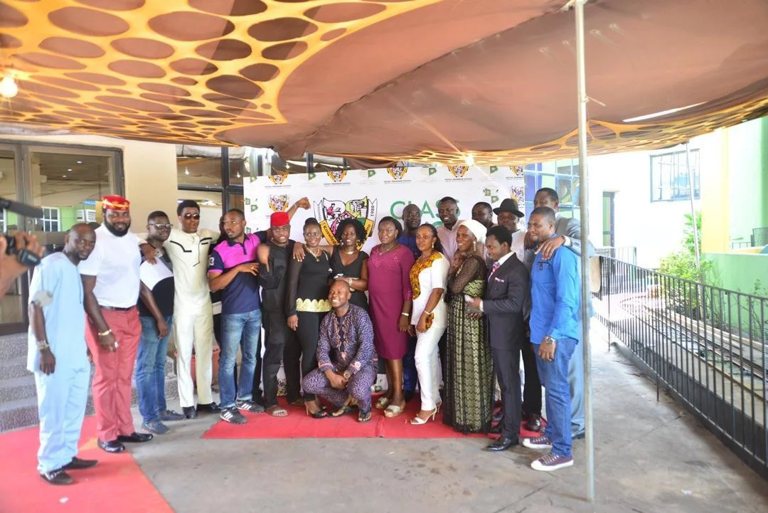 A large group of Class of 1998 members standing together on a red carpet under a canopy in front of the Festac Grammar School crest backdrop at Frank Kids Park, 20 March 2016.
