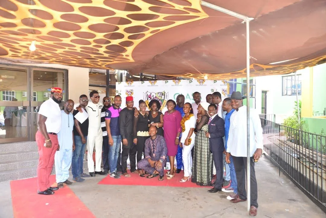 Members of the Class of 1998 posing as a group beneath the canopy in front of the school crest backdrop during the inaugural gathering.