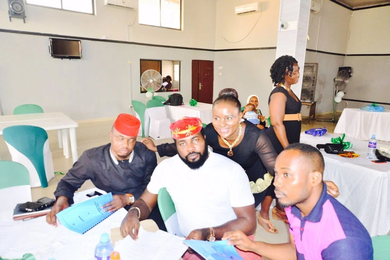 Members seated at a table in the hall at Frank Kids Park holding bound blue documents, with others standing behind them.