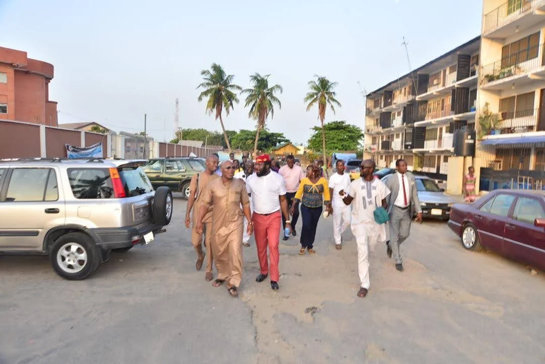 Members walking together along a Festac Town street lined with parked cars, palm trees and apartment blocks, on their way to Festac Grammar School.