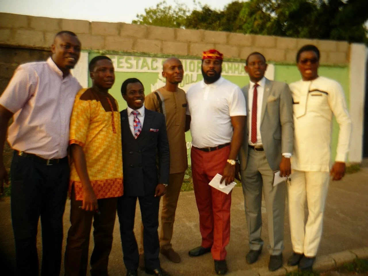Seven members standing together in front of the Festac Senior Grammar School wall during the visit on the day of the inaugural meeting.