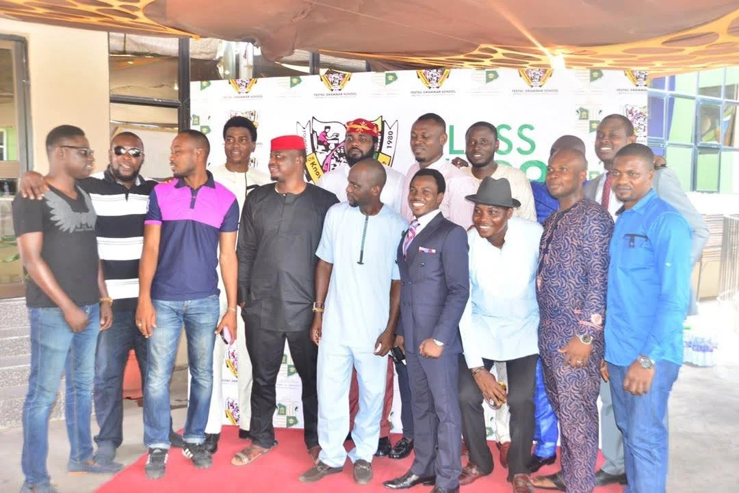 A group of male members standing together on the red carpet in front of the school crest backdrop during the inaugural gathering.