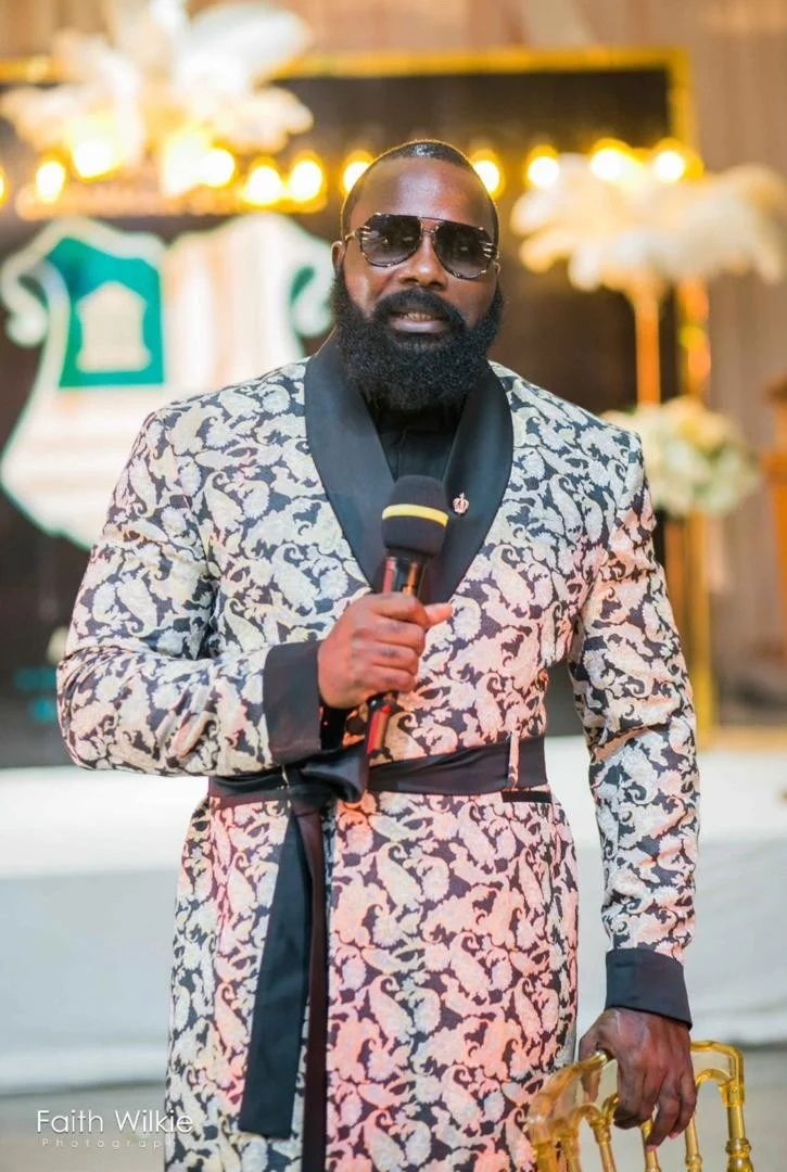 A member speaking into a microphone before the Festac Grammar School crest during the 2020 Homecoming programme.