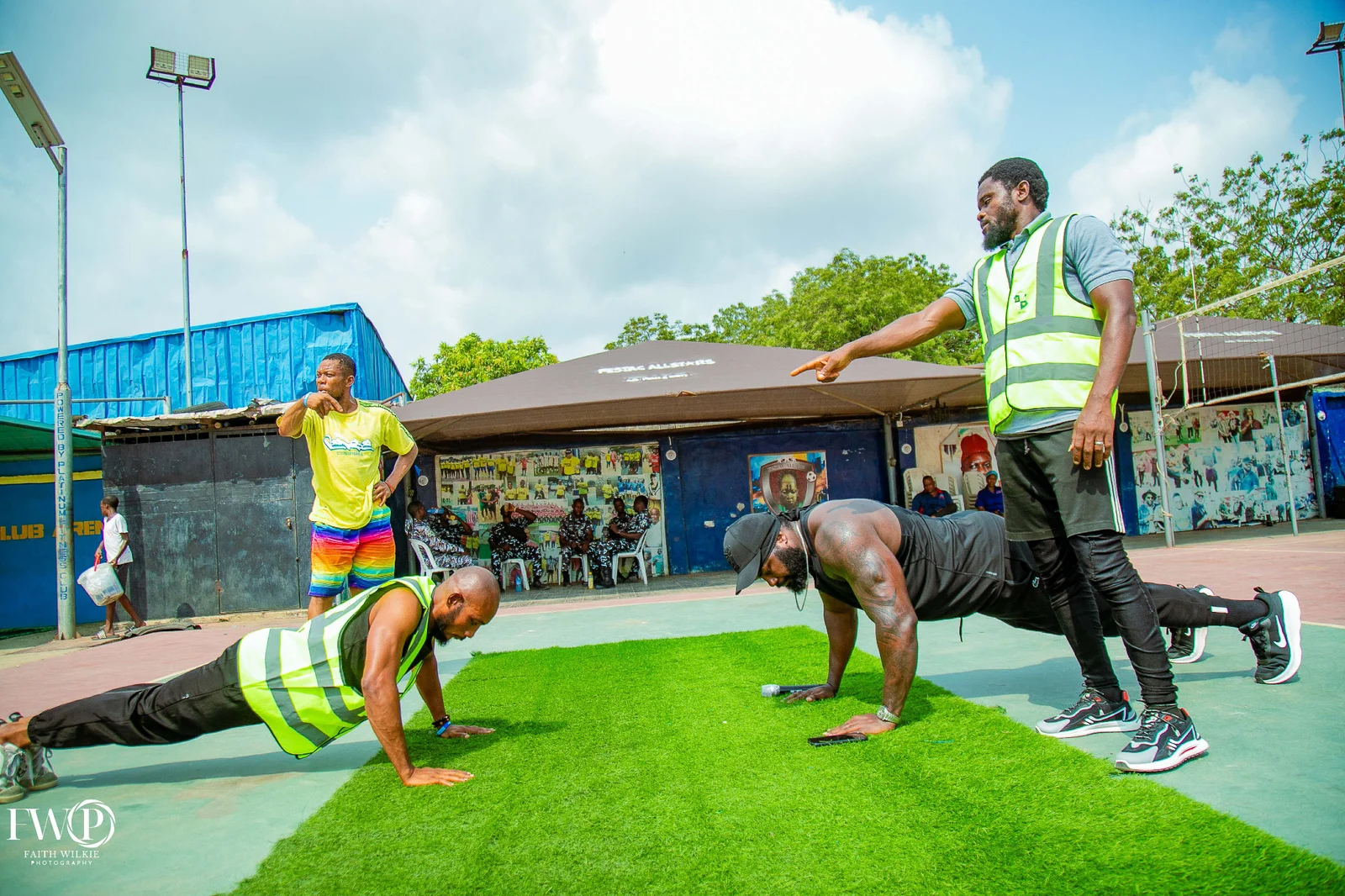 Participants doing push-ups on artificial turf while a member judges during the 2025 Homecoming fitness activities.