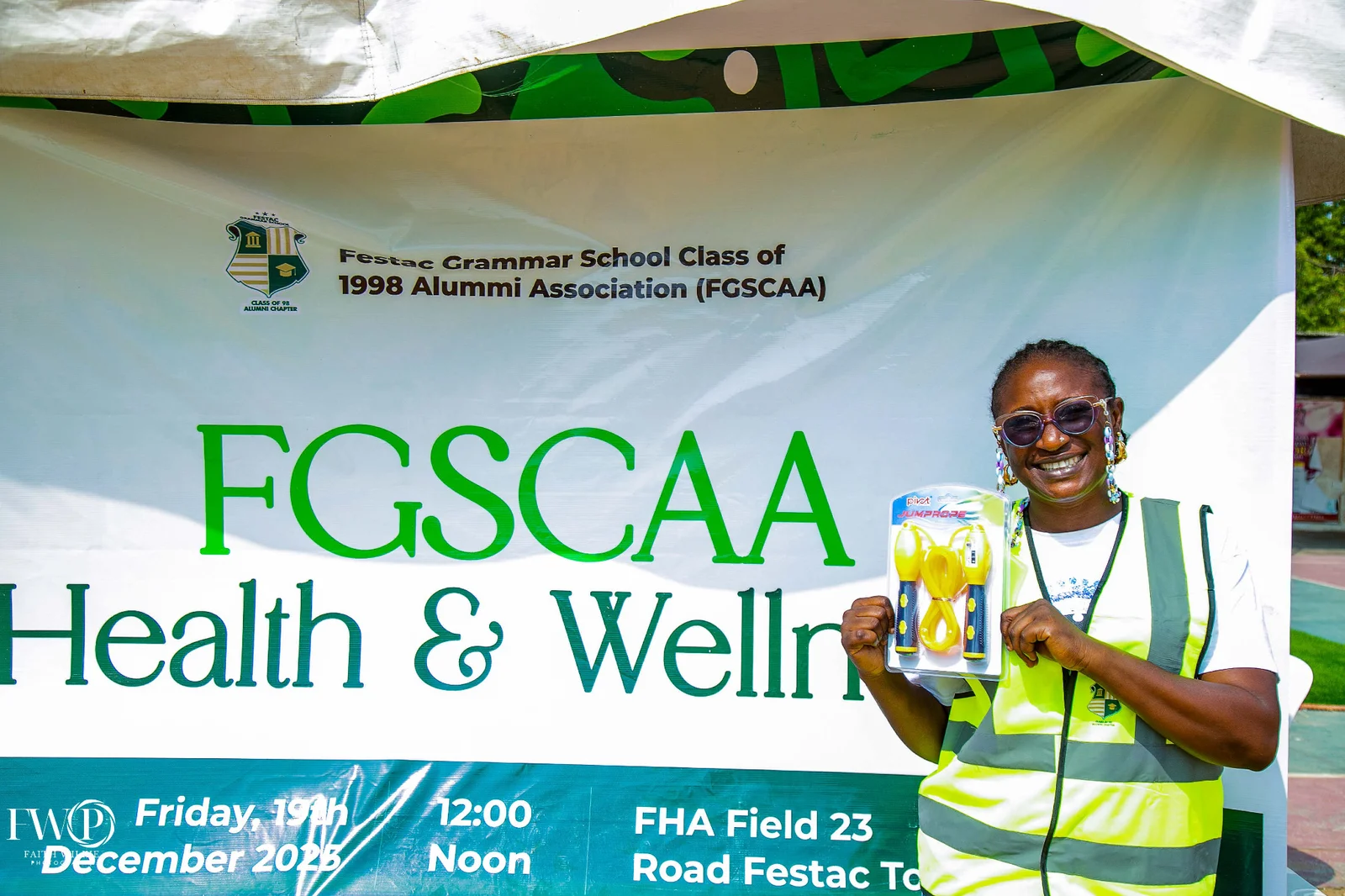 An FGSCAA member holding a jump-rope prize beside the FGSCAA Health & Wellness banner at FHA Field.