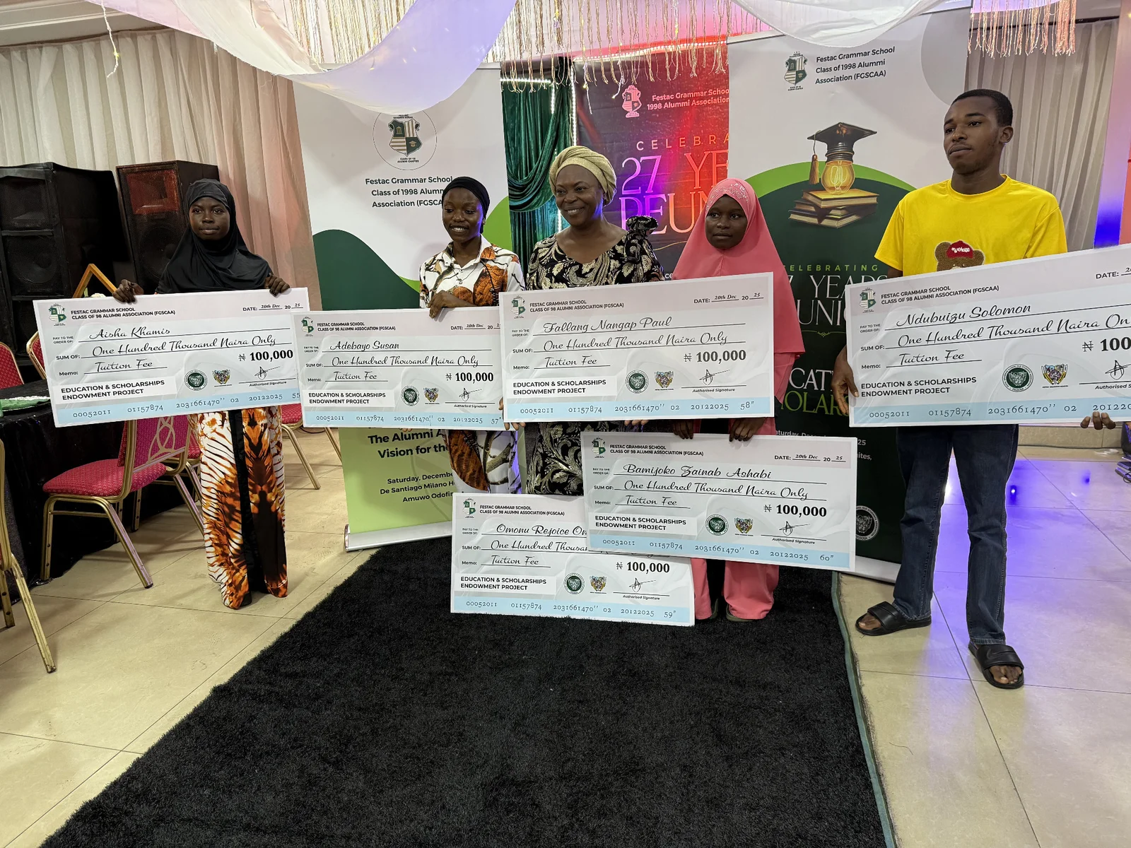 Six scholarship recipients holding FGSCAA tuition-support cheques in front of the 27 Years Reunion backdrop on 20 December 2025.