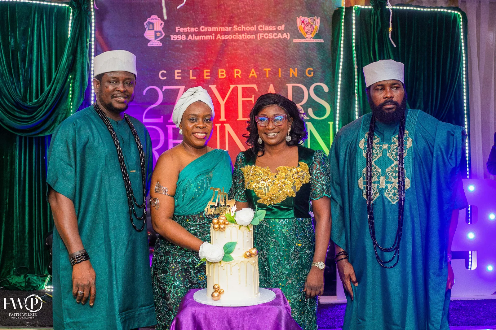 Four FGSCAA members in green attire standing behind a 27th anniversary cake in front of the Celebrating 27 Years Reunion backdrop.