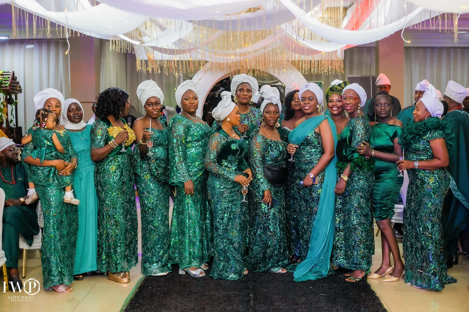A group of FGSCAA members in green sequinned attire and white head-wraps standing together beneath draped ceiling decorations at the reunion dinner.