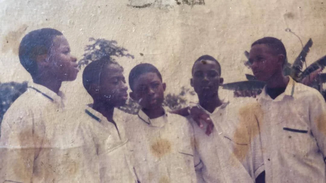 A faded and water-stained print of five male students in white school shirts standing together outdoors.