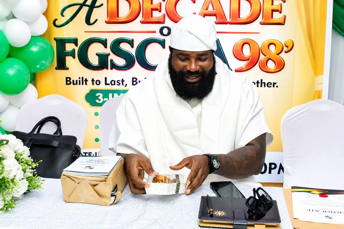 A member seated at the high table opening a gift box beneath the “A Decade of FGSCAA 98’” banner