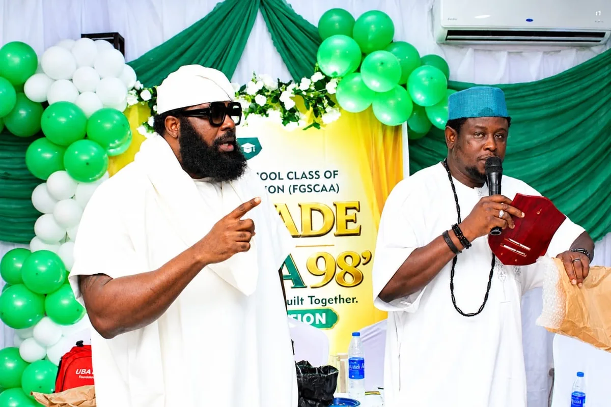 A member speaking and pointing while another holds a microphone and a plaque in front of the anniversary backdrop