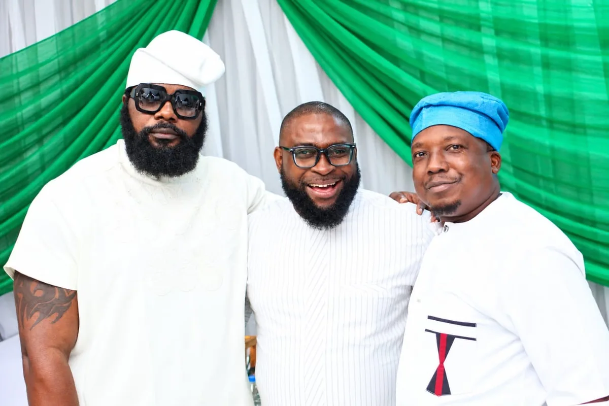 Three members smiling with arms around each other in front of green and white drapes