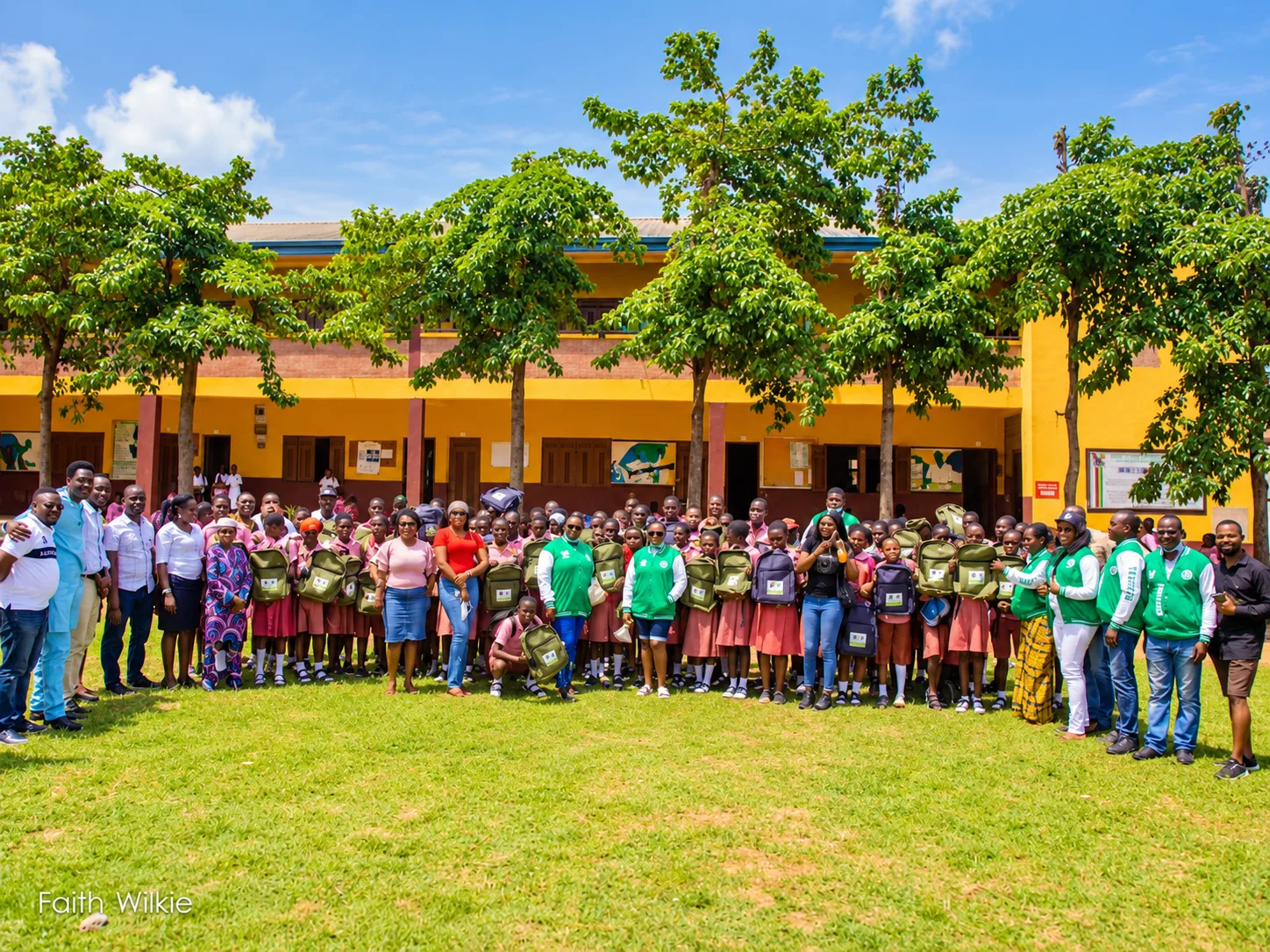 Group photo of students holding new backpacks with FGSCAA members during the 2021 Back-to-School Programme, in front of a school building.