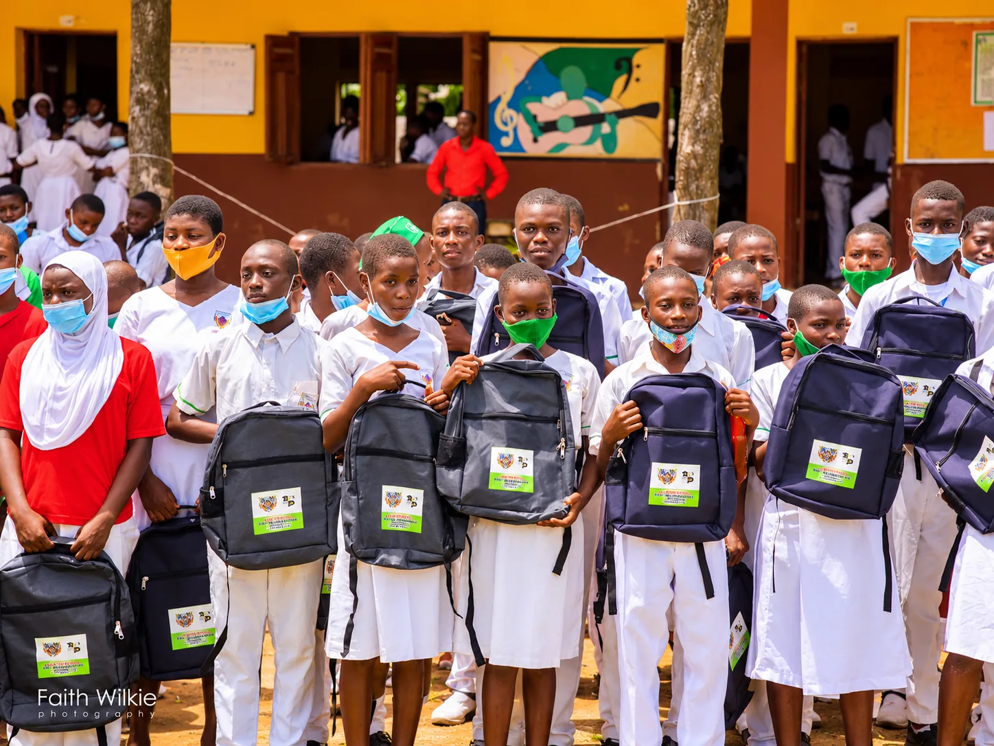 Students in school uniform holding their new donated backpacks.