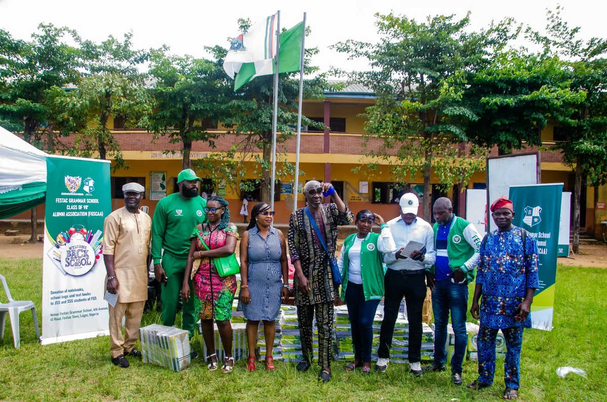 FGSCAA members and school representatives stand on the school field in front of stacked notebooks, beside a Back-to-School banner and the school flagpoles.