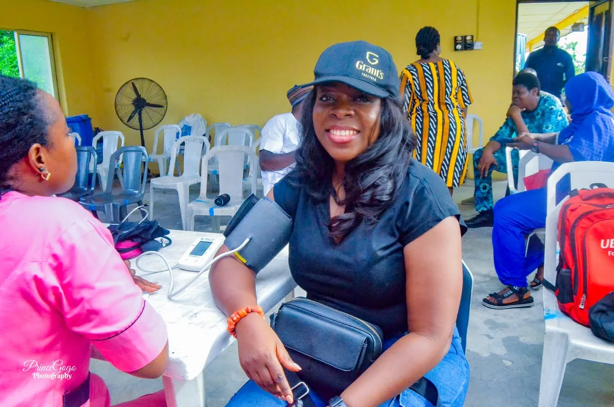 A participant smiles while wearing a blood-pressure cuff as a health worker in pink scrubs takes a reading at the 2024 free medical check-up.