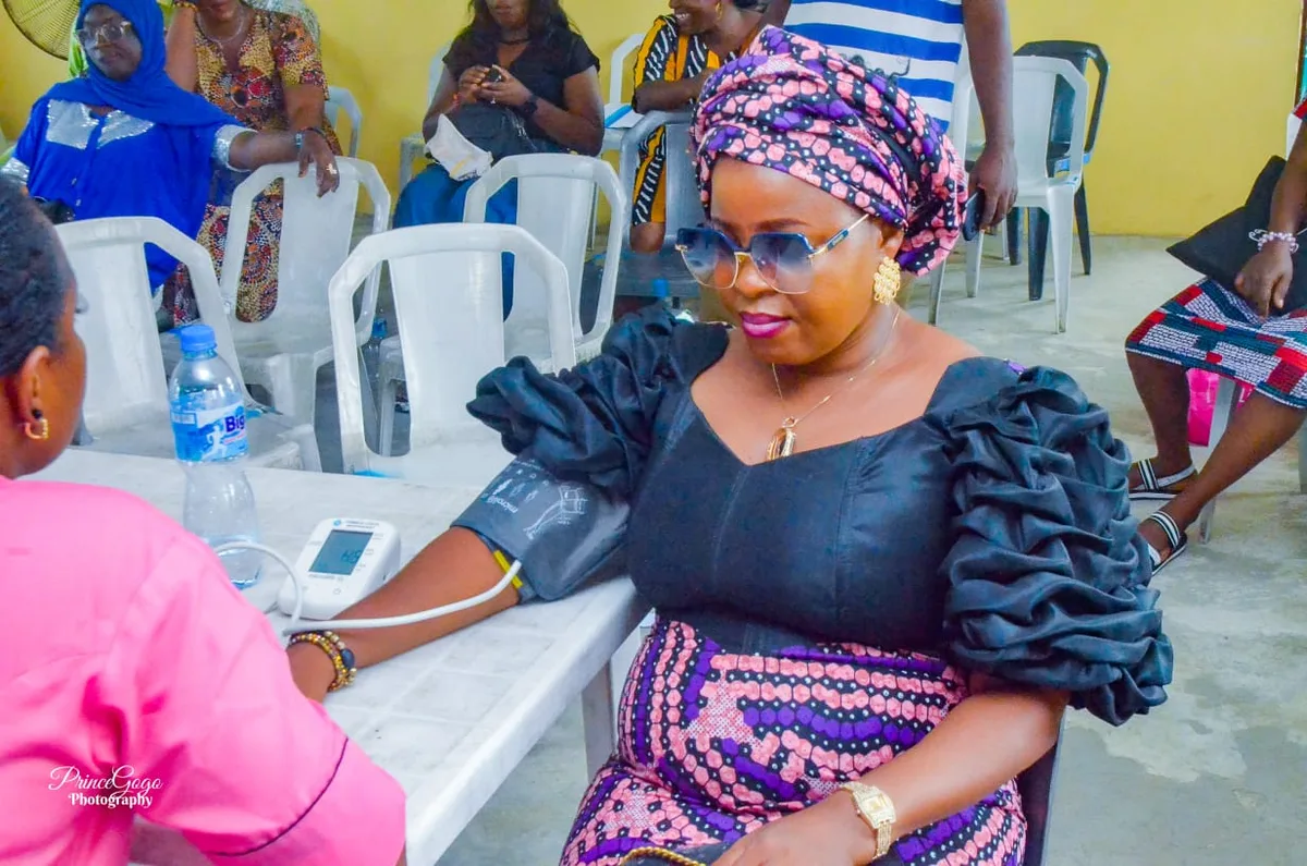 A participant in a patterned headwrap sits with a blood-pressure cuff on her arm as a digital monitor takes a reading.