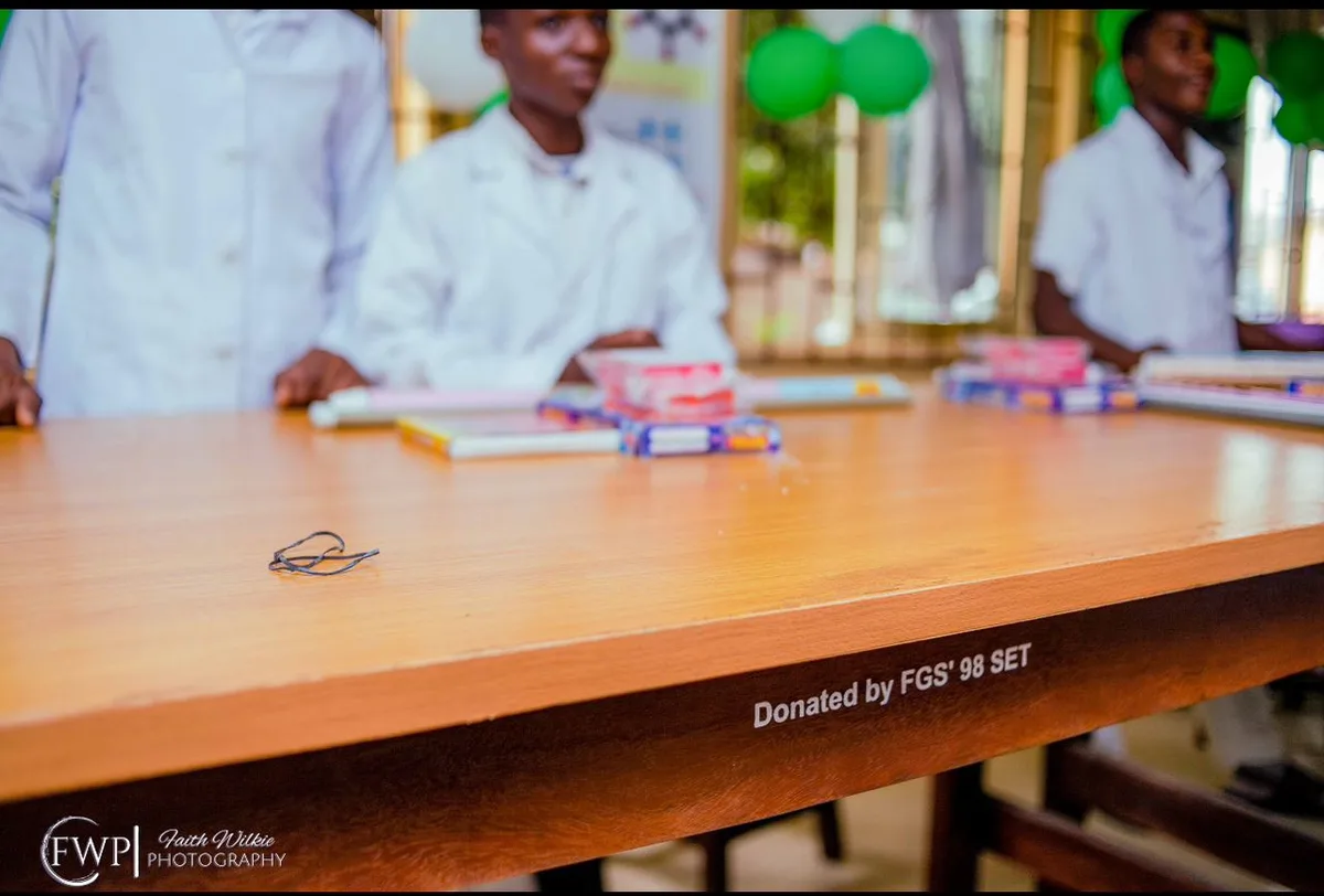 Edge of a laboratory workbench bearing the marking “Donated by FGS ’98 Set”, with students in lab coats in the background.