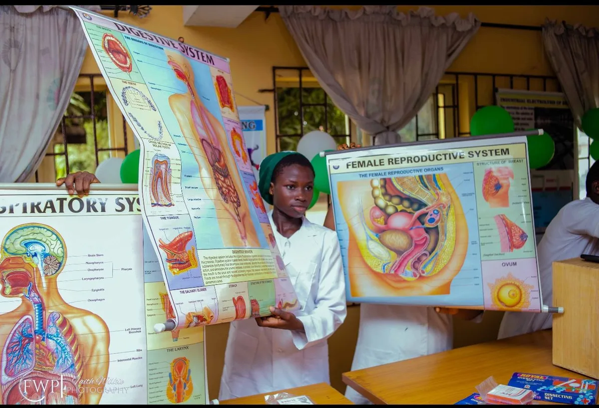 Students holding up biology teaching charts of the digestive, respiratory and female reproductive systems.