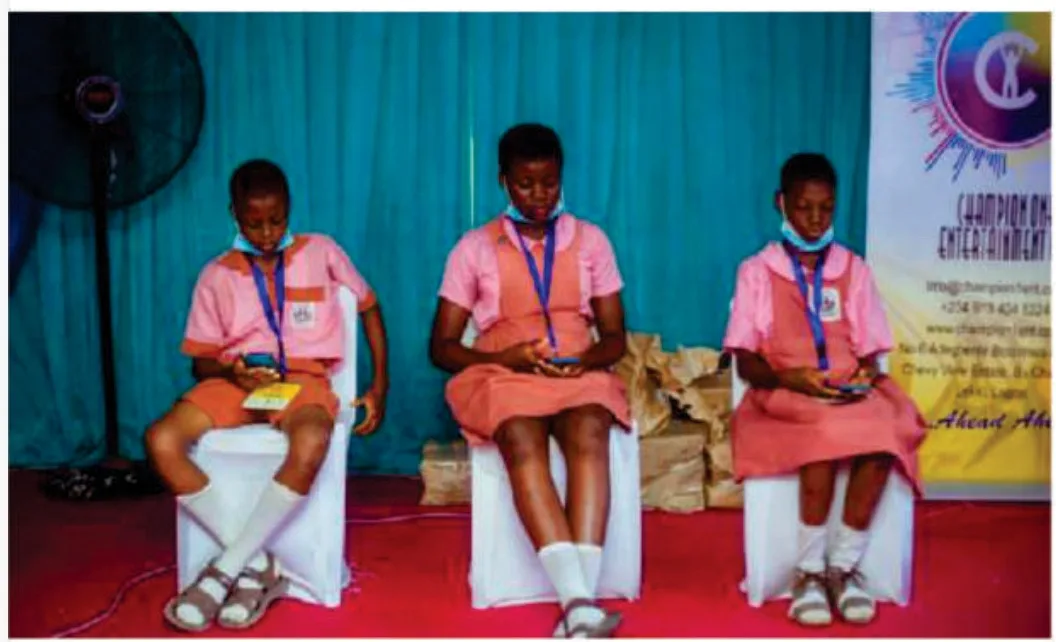Three students in pink school uniforms seated on stage during the 2021 Spelling Bee competition.