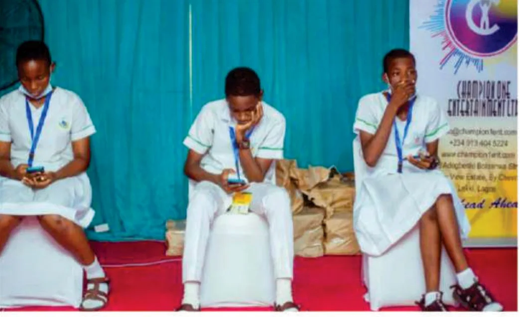 Three students in white school uniforms seated on stage during a competitive stage of the 2021 Spelling Bee.