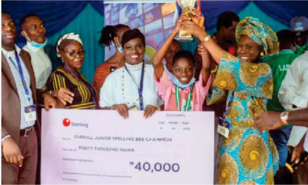 The Overall Junior Spelling Bee Champion raising a trophy beside a ₦40,000 prize cheque during the 2021 competition.