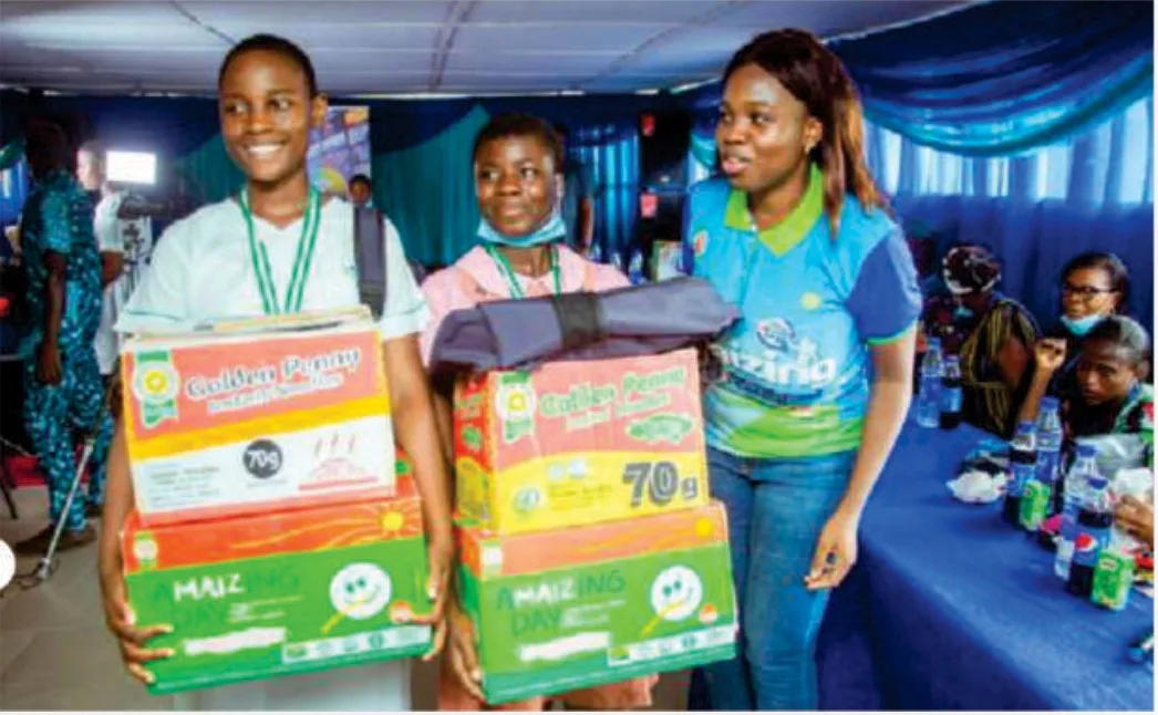 Two students carrying boxed educational support prizes alongside an event representative.